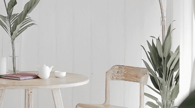 Wooden table and chair with plants in front of white wall